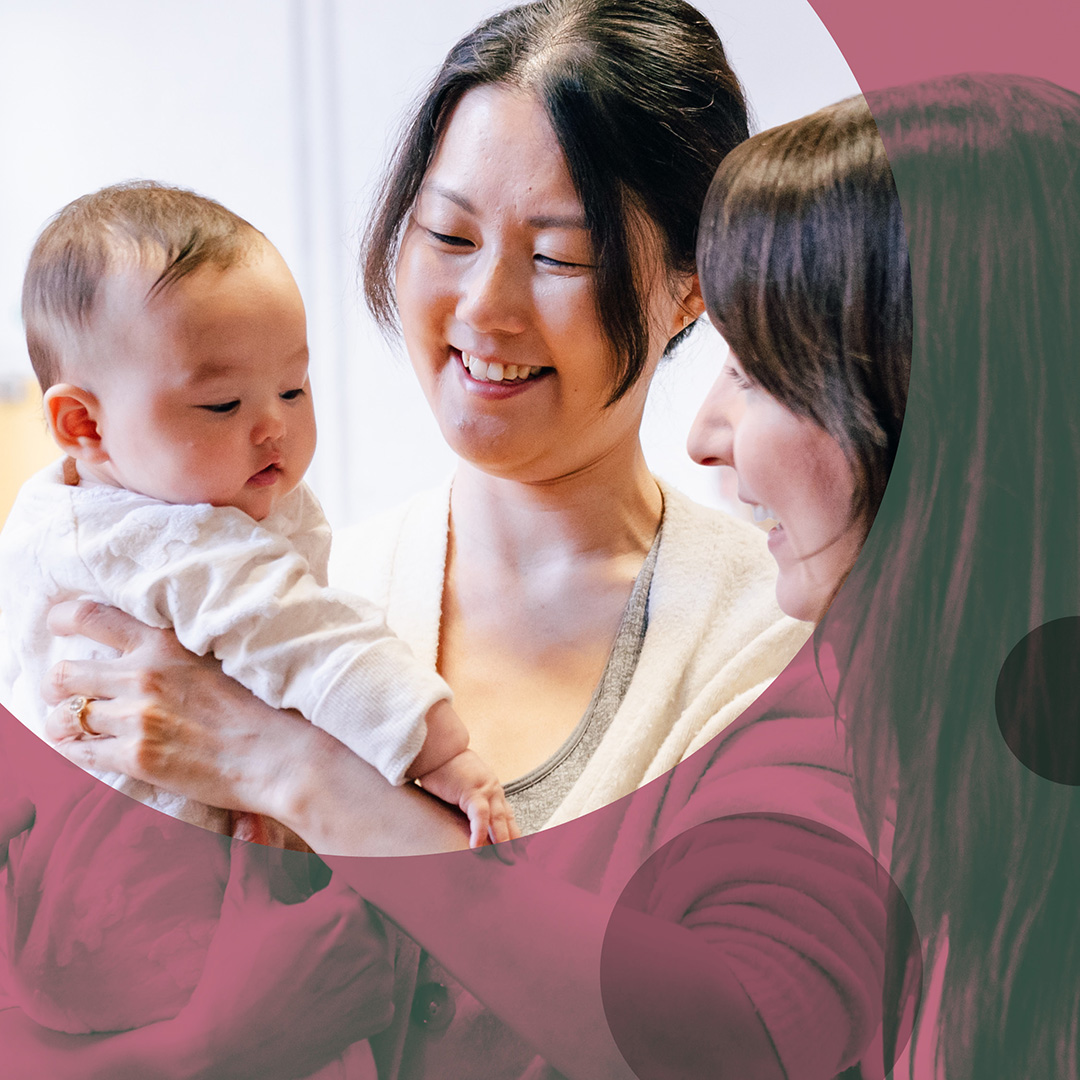 Smiling parent holding a baby with another smiling parent looking on