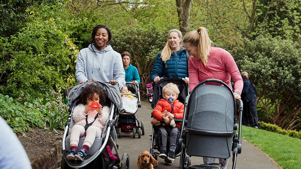 Mums walking in a park pushing their children in buggies