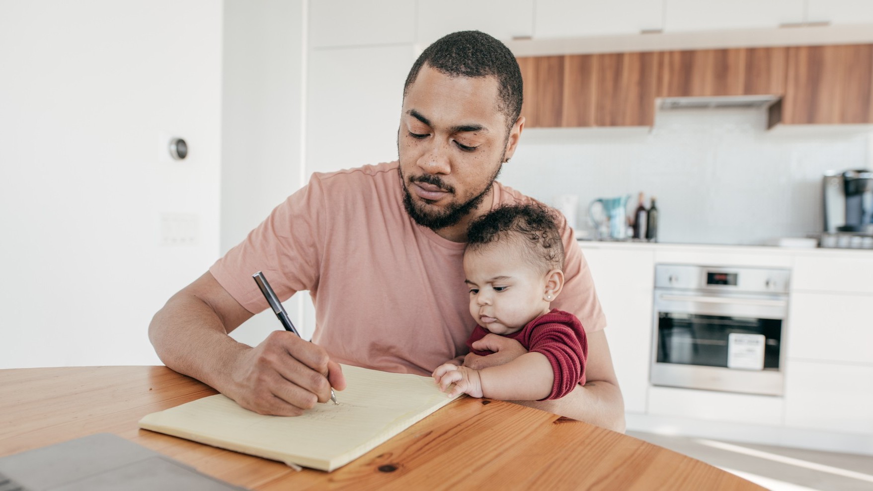 Dad holding baby while writing at table