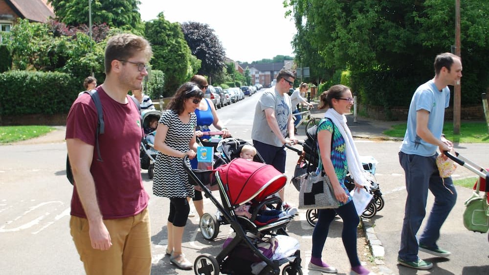 Parents pushing buggies across the road in a walking group