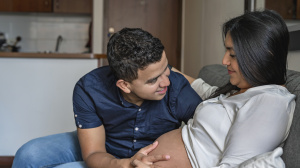 Couple sitting on sofa, cradling pregnant tummy