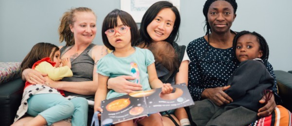 Three mums reading books to their daughters