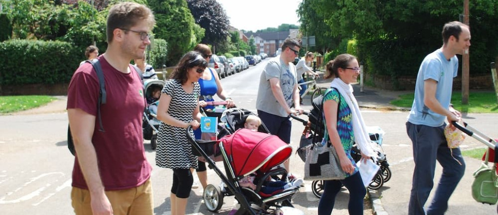 Parents pushing buggies across the road in a walking group